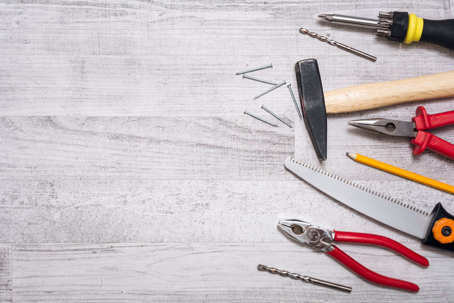 Tool Set of Hammer, Nails, Screwdriver, Pliers, Pen and a Saw on a Wooden Table - Top down View with Copy Space